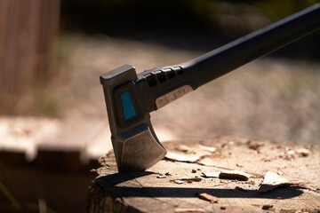 An axe with a steel blade stuck into a stump against a blurred background. There are splinters from...