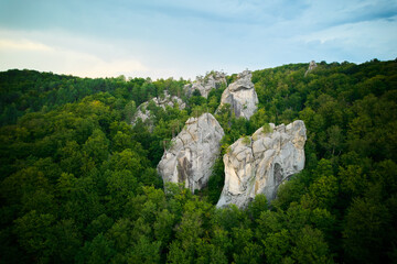 Aerial view of rock formations surrounded by dense, lush green forests. Contrast between rocky...