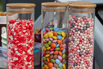 Jars filled with red, pink, and pastel-colored candies stand prominently at a festive outdoor gathering, showcasing a variety of treats for visitors to enjoy