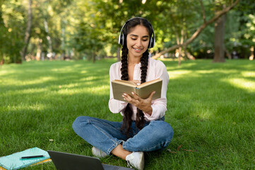 Enjoying free time. Happy indian lady reading interesting book and wearing wireless headphones,...
