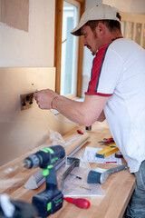 Kitchen Fitters: Electrical Installation. An electrician working on a plug socket mounted into a splashback of a new kitchen build. From a series of related images.