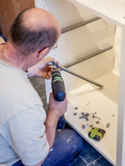 Kitchen Fitters: Fitting the Drawers. A worker fitting drawer runners to the carcass of a new kitchen build. From a series of related images.