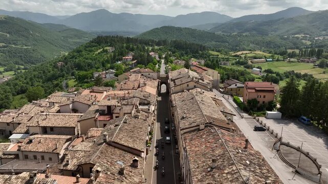 Motorcyclists Riding Through Historic Italian Town in Green Mountain Landscape