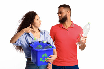 Husband Refusing To Sort Waste Having Quarrel With Wife While She Holding Box With Recycle Symbol And Plastic Litter Standing On White Studio Background. Junk Disposal, Recycling And Trash Sorting
