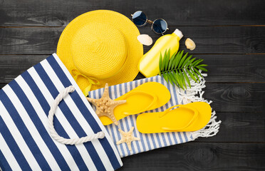 Blue beach bag with summer accessories on wooden background, top view