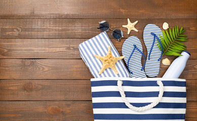 Blue beach bag with summer accessories on wooden background, top view
