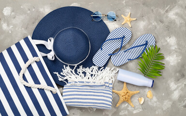 Blue beach bag with summer accessories on concrete background, top view