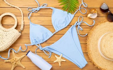 Blue bikini with beach accessories on wooden background, top view