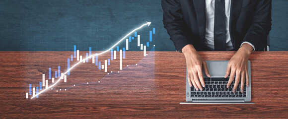 A businessman in a suit is intently working on a laptop, analyzing a financial graph representing...