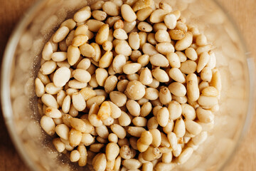Top view of glass jar with pine nuts on wooden table, close-up.