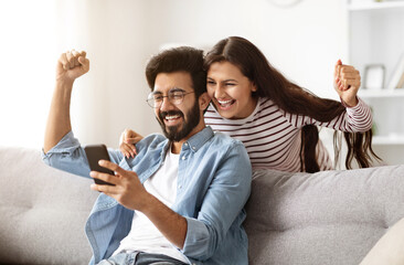 Fototapeta na wymiar Great news. Excited happy millennial indian man and woman looking at phone screen, clenching fists and exclaiming. Emotional eastern couple celebrating success, gambling online. Cashback