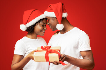 African american lovers in Santa hats having magic moment during New Year celebration, touching...