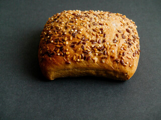 One small roll with grain and seeds on dark background. Fine bakery product made from high quality...