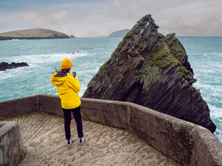 Girl tourist in yellow jacket and hat explore stunning Dunquin Pier area in county Kerry, Ireland....