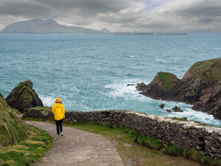 Girl tourist in yellow jacket and hat explore stunning Dunquin Pier area in county Kerry, Ireland....