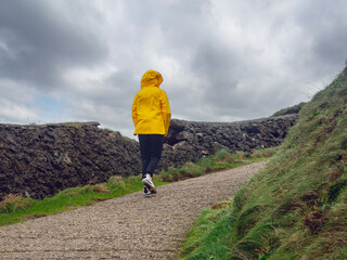 Girl tourist in yellow jacket and hat explore stunning Dunquin Pier area in county Kerry, Ireland....