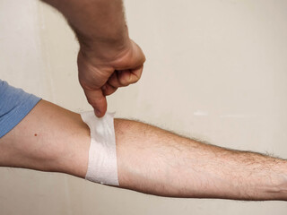 Mans arm pulling off old used bandage, dirty wall background. Dangerous accident on a construction...