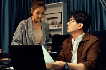 Managers discussing on document paperwork together for business planning on market share data at over late night time at modern home office, working on startup company deadline project job. Infobahn.