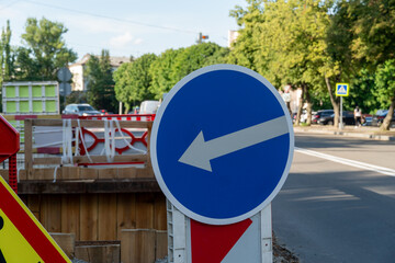 Traffic sign indicating left turn direction on a city street during daytime with trees and vehicles...
