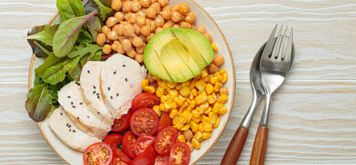 Healthy bowl with grilled chicken breast, avocado, chickpeas, corn, tomatoes and mixed greens, top...