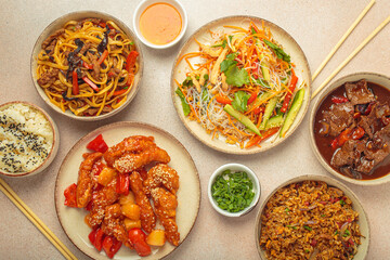 Assorted Chinese dishes, sweet and sour chicken, beef in sauce, noodles, fried rice, salad and wooden chopsticks. Chinese or Asian restaurant concept