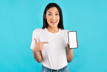 I Recommend. Amazed young woman pointing at blank phone screen over blue studio wall