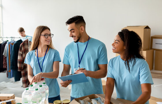 Arab male manager checking donation list and writing in clipboard. Diverse volunteer workers working in shipping delivery charitable stock organization packing donations boxes