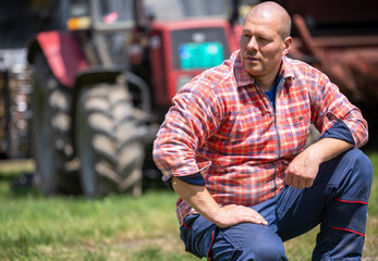 Male farmer posing in plaid shirt near tractor on sunny day