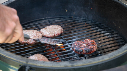 Grilling hamburger patties on an outdoor, charcoal grill.