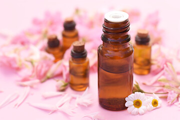 Essential oil bottles on pink flowers background, selective focus, shallow DOF