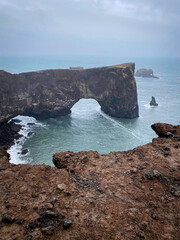 Scenic view of the natural rock arch at Dyrhólaey, Iceland, with sea stacks rising from the...