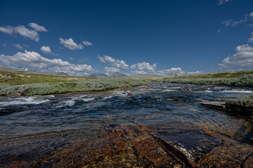 Summer in Norway, shallow river flowing through the highlands, vast blue sky and summer clouds,...