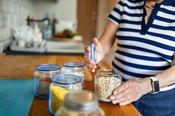Senior woman using glass jars to store food at home kitchen

