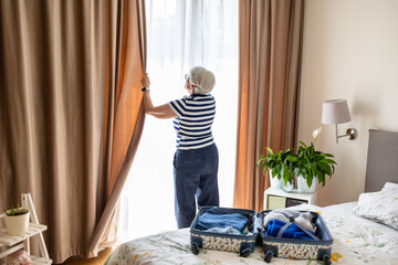 Senior woman closing the curtains on a window in a hotel room
