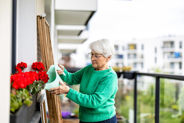 Senior woman watering flowers on balcony of her house
