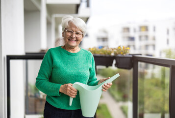 Senior woman watering flowers on balcony of her house
