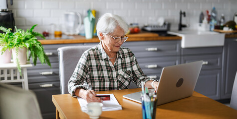 Senior woman using laptop and credit card for online shopping at home

