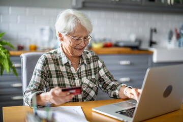 Senior woman using laptop and credit card for online shopping at home

