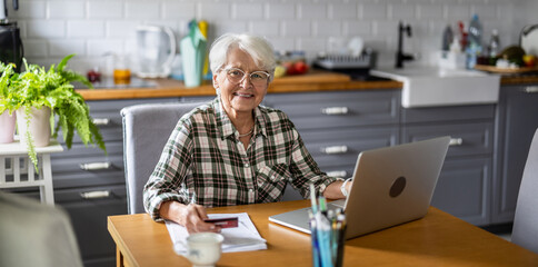 Senior woman using laptop and credit card for online shopping at home


