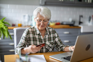 Senior woman using laptop and credit card for online shopping at home

