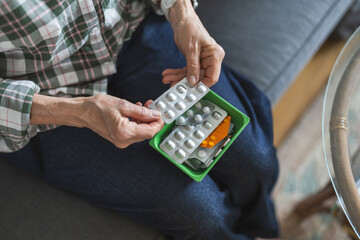 Unrecognizable elderly woman taking her medication at home, close-up of woman’s hands

