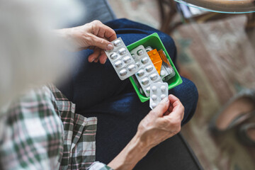 Unrecognizable elderly woman taking her medication at home, close-up of woman’s hands
