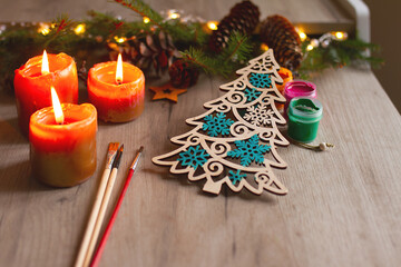 Winter painted wooden toy Christmas tree with brushes, paints, spruce branches, pinecones and candles on table