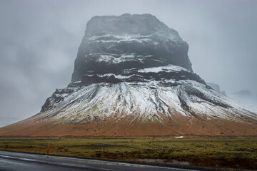 Steeply rising table mountain Lómagnúpur seen from Iceland’s Ring Road No. 1, with wet asphalt...
