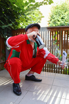 Elderly man dressed in tracksuit, squatting with beer and cigarette, comic Slavic gopnik pose.