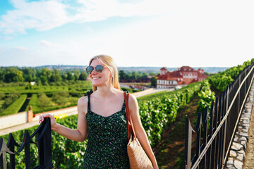Happy female tourist in green dress posing near scenic vineyard and historic estate.