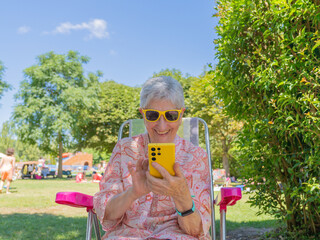 Senior woman happily embracing technology in a park, using her mobile phone and enjoying retirement