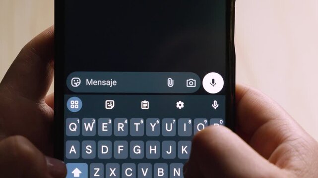 Close-up of a hand using a smartphone, showing the message "Hola!" typed on the screen in a messaging app.