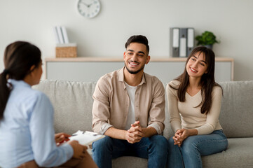 Family therapy. Happy middle eastern couple sitting on couch at counselor's office, listening advices and smiling. Effective marital therapy concept