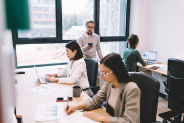 Office team working independently on laptops and reports in open coworking space, showcasing quiet focus, productivity and efficient task management in creative tech environment